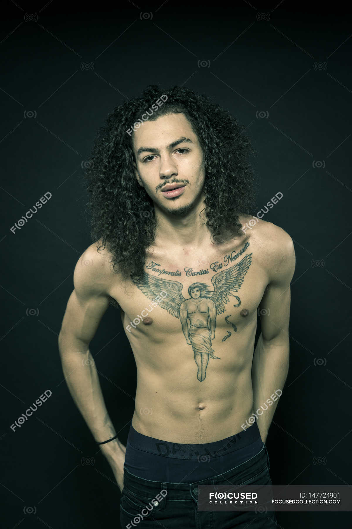 Portrait of man with tattooed chest and long hair — confident, black background - Stock Photo