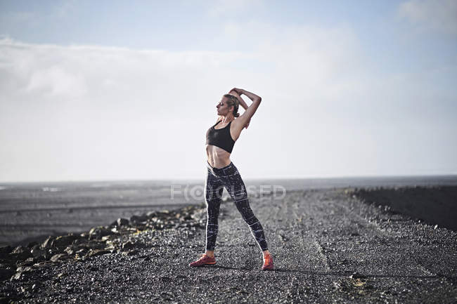Woman stretching on deserted unmade road — Stock Photo