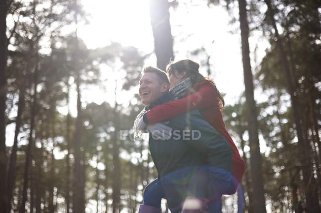 Man gives woman piggy back in woods — Stock Photo