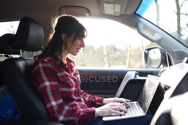 Donna seduta in auto e utilizzando il computer portatile — Foto stock