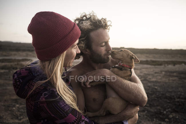 Casal segurando cão na praia — Fotografia de Stock