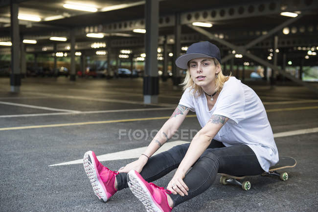 Fille patineuse tatouée assis sur skateboard — Photo de stock