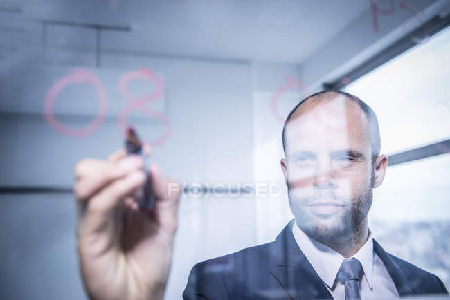 Hombre de negocios escribiendo números en vidrio - foto de stock