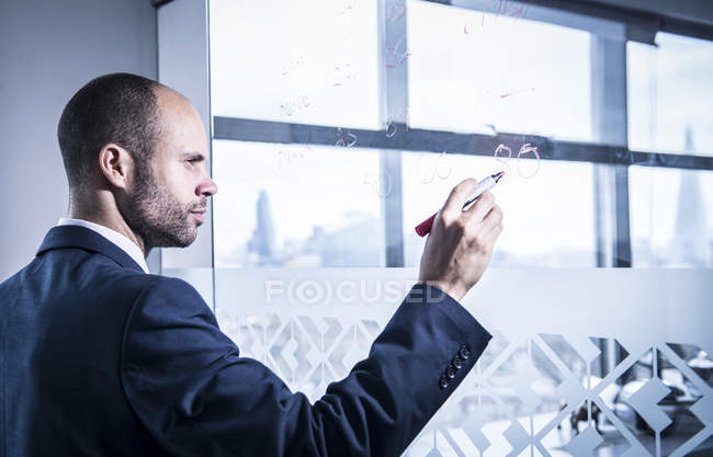 Hombre de negocios escribiendo números en vidrio - foto de stock