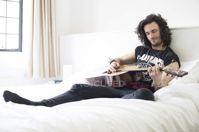 Man playing guitar in bed — Stock Photo