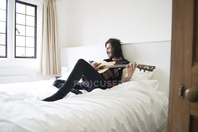 Homme couché sur le lit et jouant à la guitare — Photo de stock