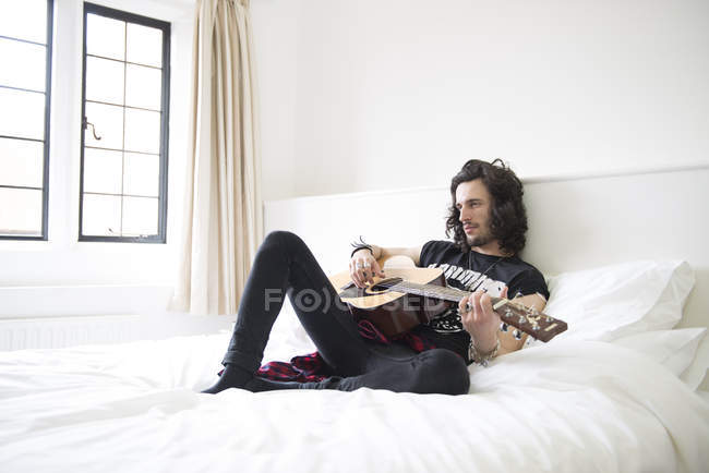 Homem deitado na cama e tocando na guitarra — Fotografia de Stock