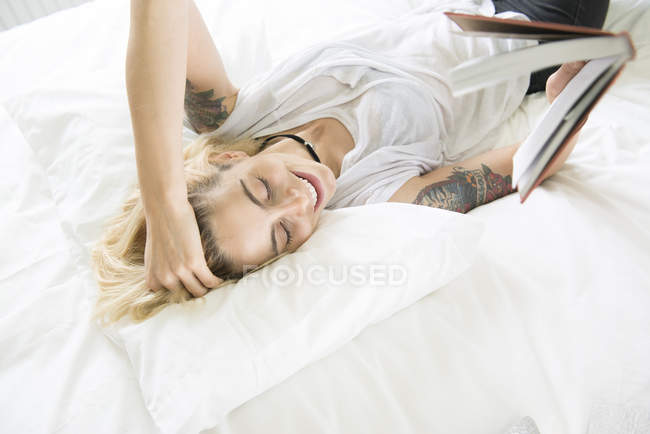 Frau mit Tätowierungen liegt auf Bett und liest — Stockfoto
