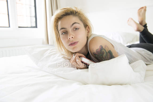 Mujer con tatuajes acostada en la cama con libro - foto de stock