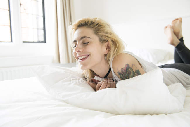 Frau mit Tätowierungen liegt mit Buch im Bett — Stockfoto