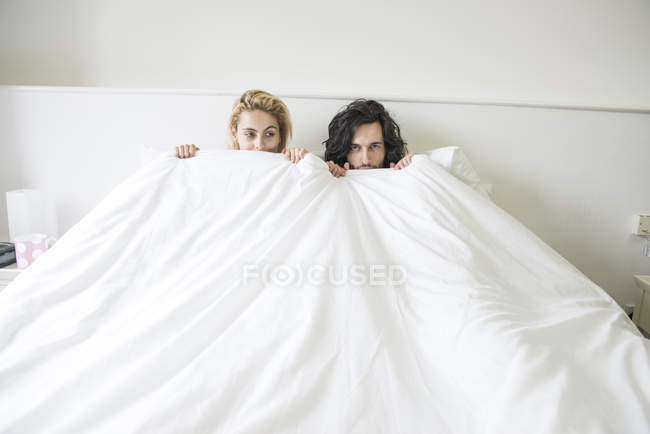Пара в постели, играющая в прятки с камерой — стоковое фото