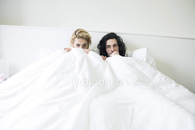 Casal na cama jogando peekaboo com câmera — Fotografia de Stock