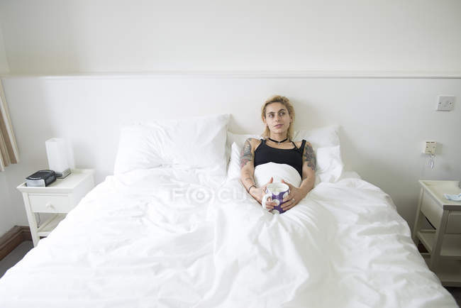 Жінка лежить в ліжку і насолоджується чашкою чаю — стокове фото