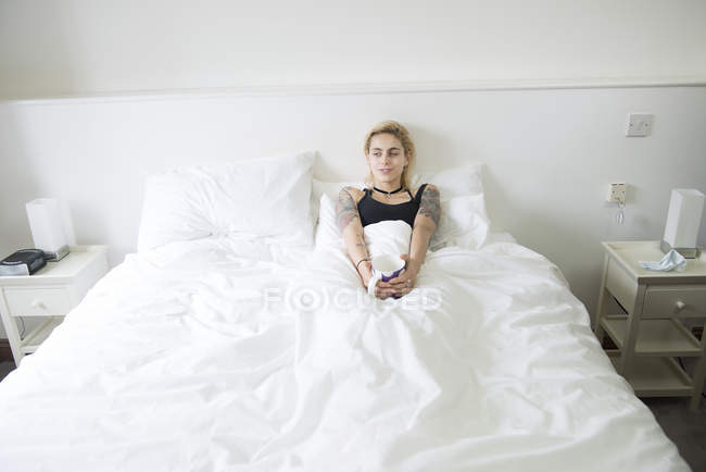 Femme couchée au lit et profitant d'une tasse de thé — Photo de stock