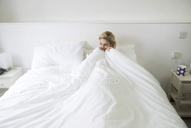 Mulher na cama com edredom puxado até o queixo — Fotografia de Stock