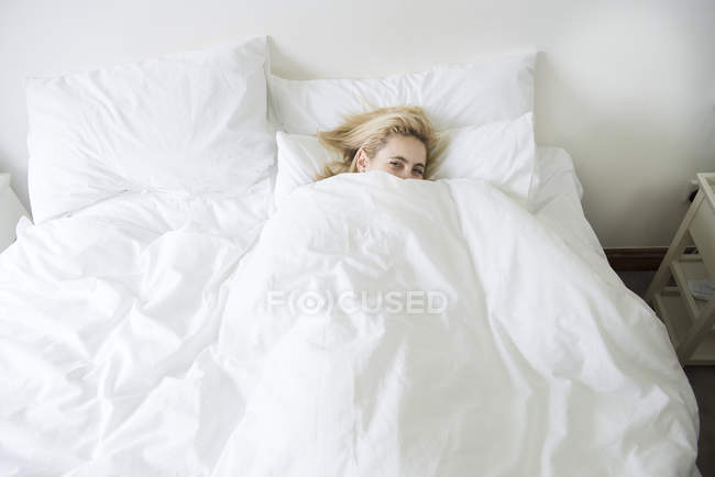 Mulher na cama com edredom puxado até o queixo — Fotografia de Stock