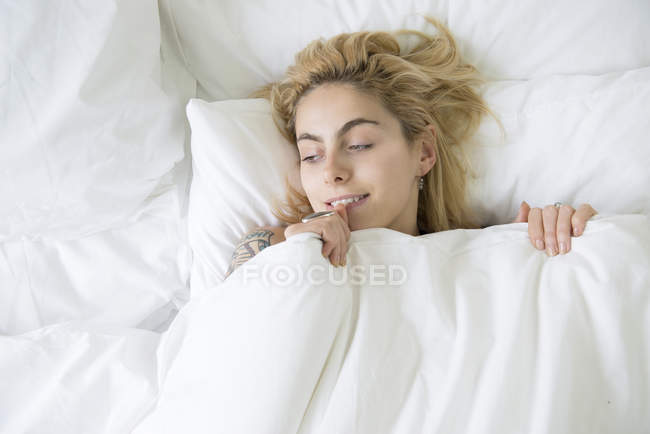 Mujer en la cama con edredón tirado hasta la barbilla - foto de stock
