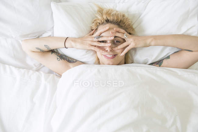 Жінка, лежачи на ліжку і охоплюють обличчя руками — стокове фото