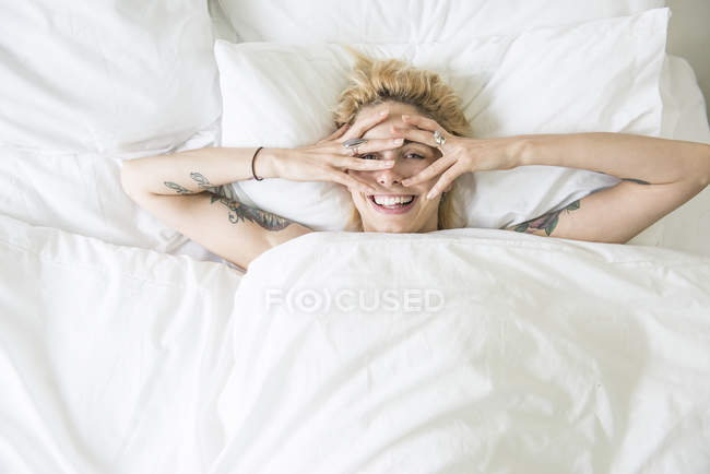 Woman lying in bed and covering face with hands — Stock Photo