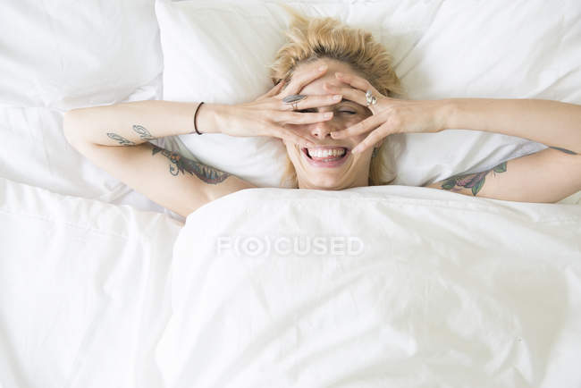 Femme couchée au lit et couvrant le visage avec les mains — Photo de stock