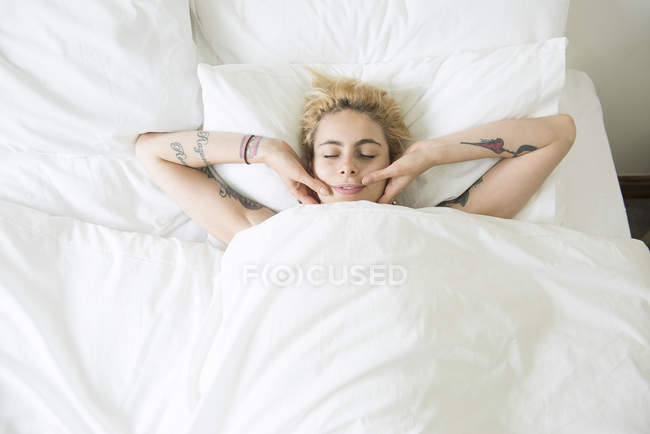 Mulher deitada na cama e cobrindo rosto com as mãos — Fotografia de Stock