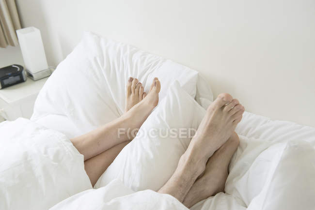 Füße ragen unter Abdeckungen hervor — Stockfoto