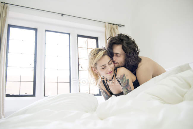 Couple tatoué câlins sur le lit — Photo de stock