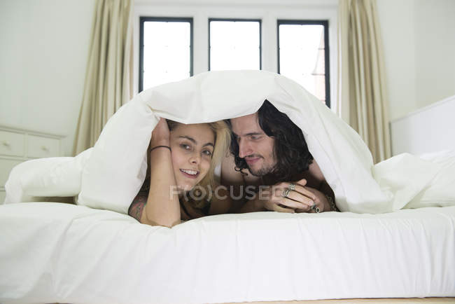 Couple peeking out from under duvet — Stock Photo