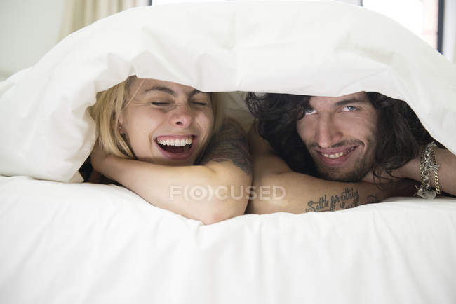Tattooed couple peeking out from under duvet — Stock Photo