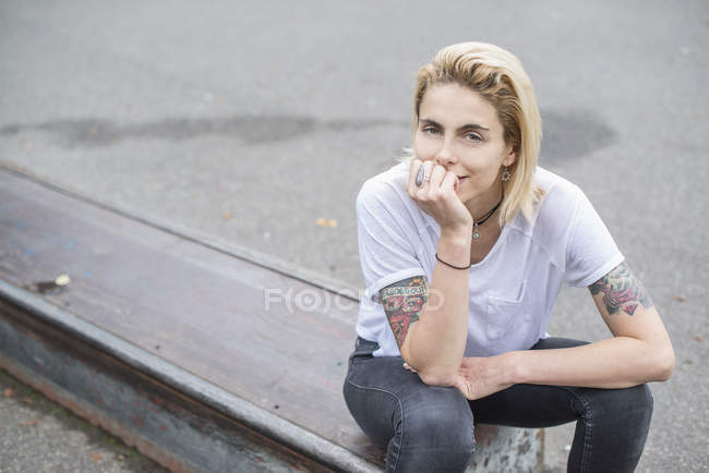 Tätowiertes blondes Mädchen sitzt im Skatepark — Stockfoto