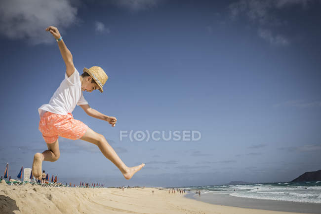 Boy jumping in sand dunes at beach — Stock Photo