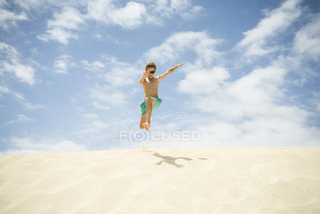 Boy jumping in sand dunes at beach — Stock Photo