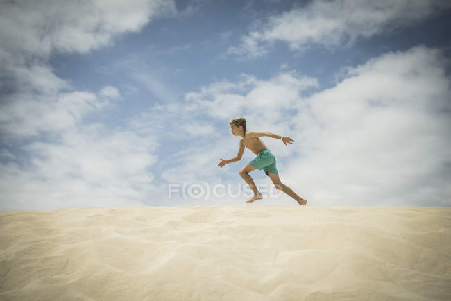 Chico corriendo en dunas de arena - foto de stock