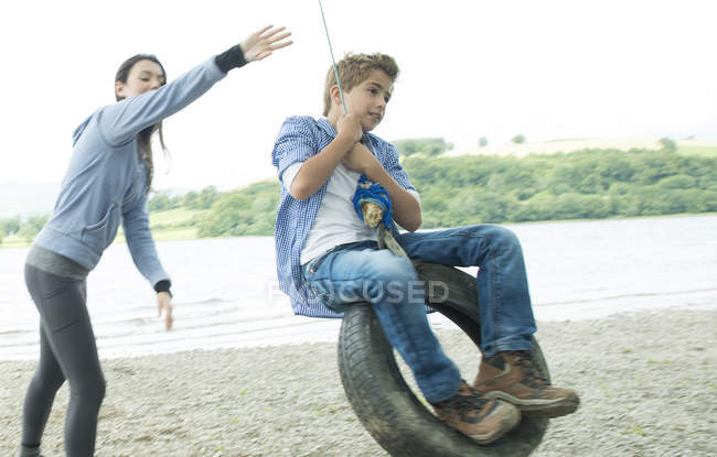 Женщина и мальчик играют на висящей на дереве шине — стоковое фото