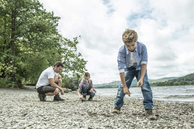 Мужчина и мальчики, скидывающие камни на берегу — стоковое фото
