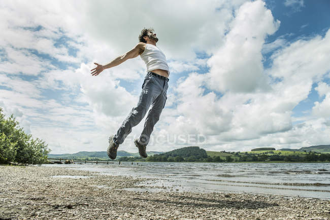 Uomo che salta in aria sulla riva — Foto stock