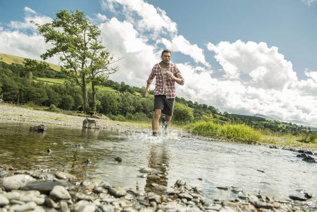 Hombre caminando a través de un río poco profundo - foto de stock