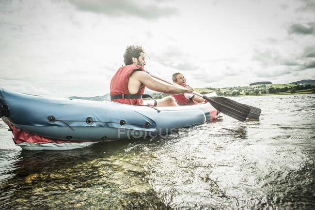 Hombre y niño en kayak remando lejos de la orilla - foto de stock