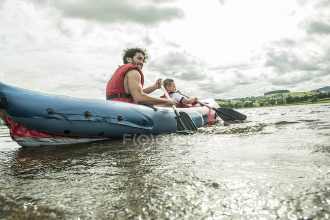 Homem e menino em caiaque remando longe da costa — Fotografia de Stock