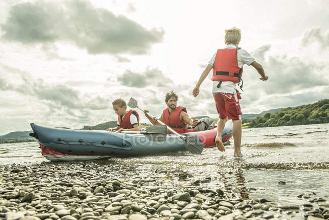 Hombre y dos chicos en kayak remando lejos - foto de stock