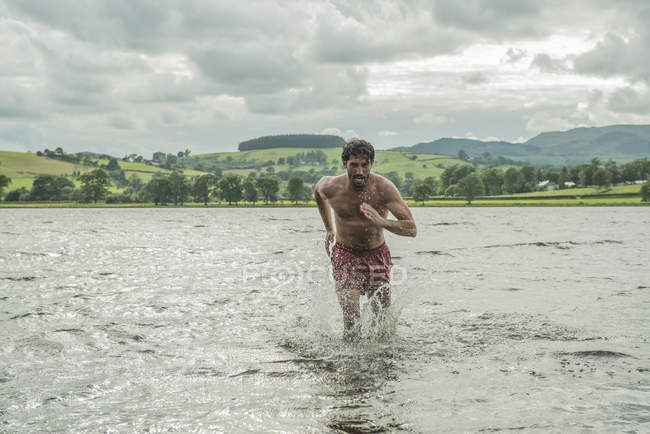 Fit man running through shallow water — Stock Photo