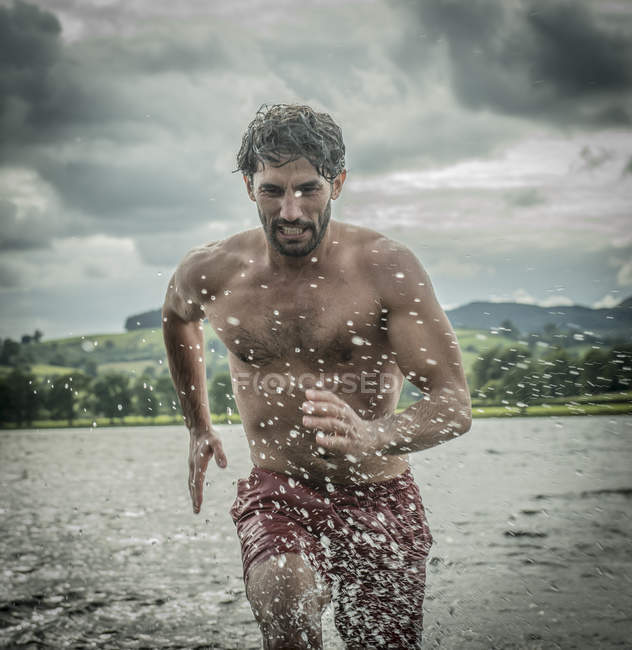 Uomo in forma che corre attraverso acque poco profonde — Foto stock