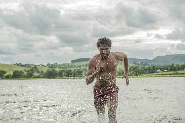 Hombre en forma corriendo a través de aguas poco profundas - foto de stock
