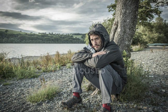 Man sitting against tree on shore — Stock Photo