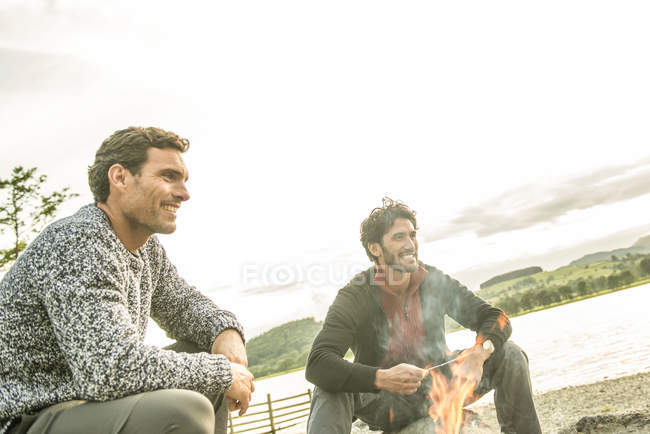 Friends relaxing around campfire on shore — Stock Photo