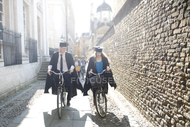 Jovens estudantes em vestidos de graduação de ciclismo — Fotografia de Stock
