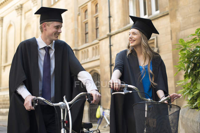 Молоді студенти у випускних сукнях їзда на велосипеді — стокове фото