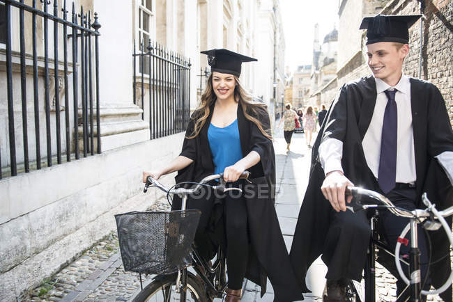Молодые студенты в выпускных платьях на велосипеде — стоковое фото