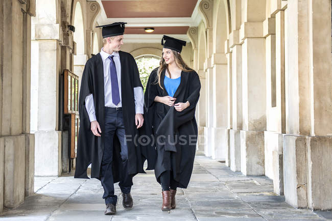 Estudiantes en vestidos de graduación caminando fuera del edificio - foto de stock