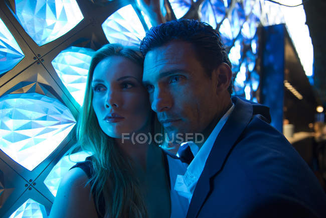 Couple bathed in blue light in front of light fixture — Stock Photo